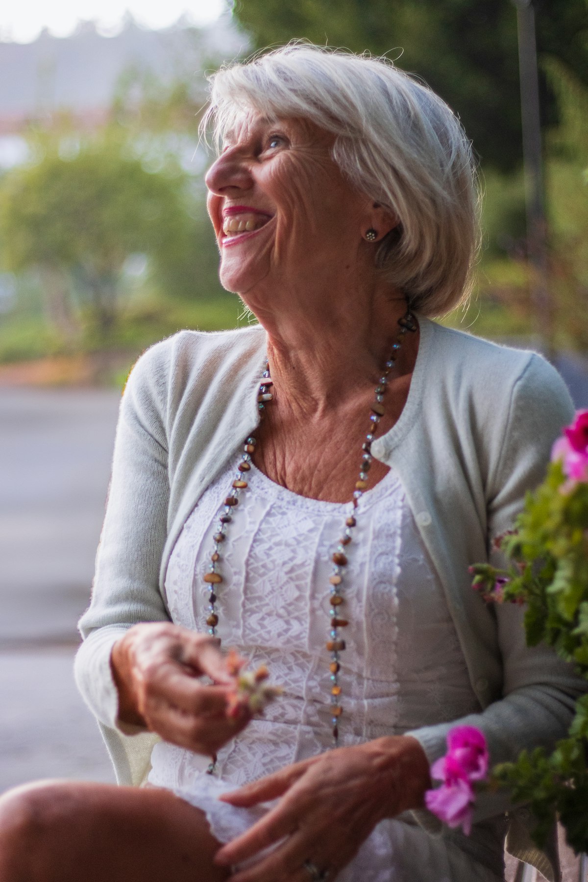 A silver-haired woman laughing outdoors with a full, natural smile